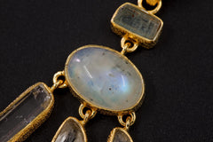 Close-up of oval Blue Moonstone and square-cut Aquamarine in a textured 18k gold-plated sterling silver pendant.
