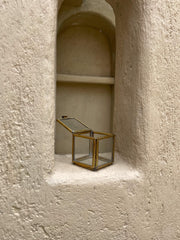 Small brass glass display box shown in a textured wall niche with clear panels and square geometric form.