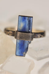 Close view of raw Kyanite ring showing indigo blade crystal, wrap-style silver setting, and hammered band texture.