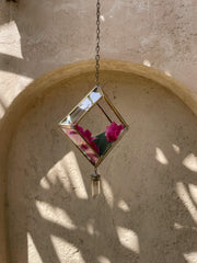 Quartz Reliquary crystal sun catcher hanging on textured wall with brass frame, glass panels, and soft natural light.