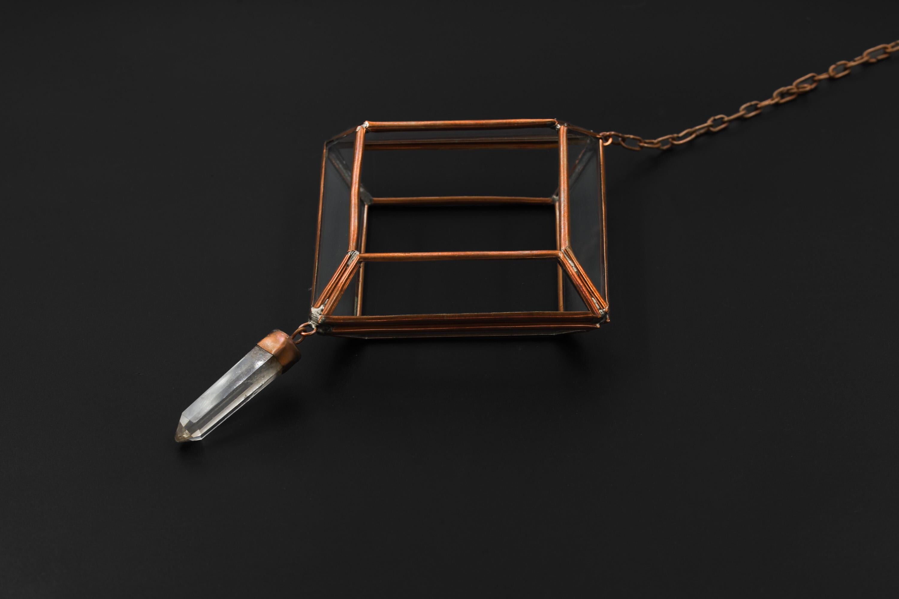 Copper Clear Quartz hanging decoration shown on dark background with geometric glass frame and raw crystal point.