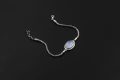 Blue Moonstone bracelet displayed on dark background with oval cabochon and detailed sterling silver Byzantine chain.
