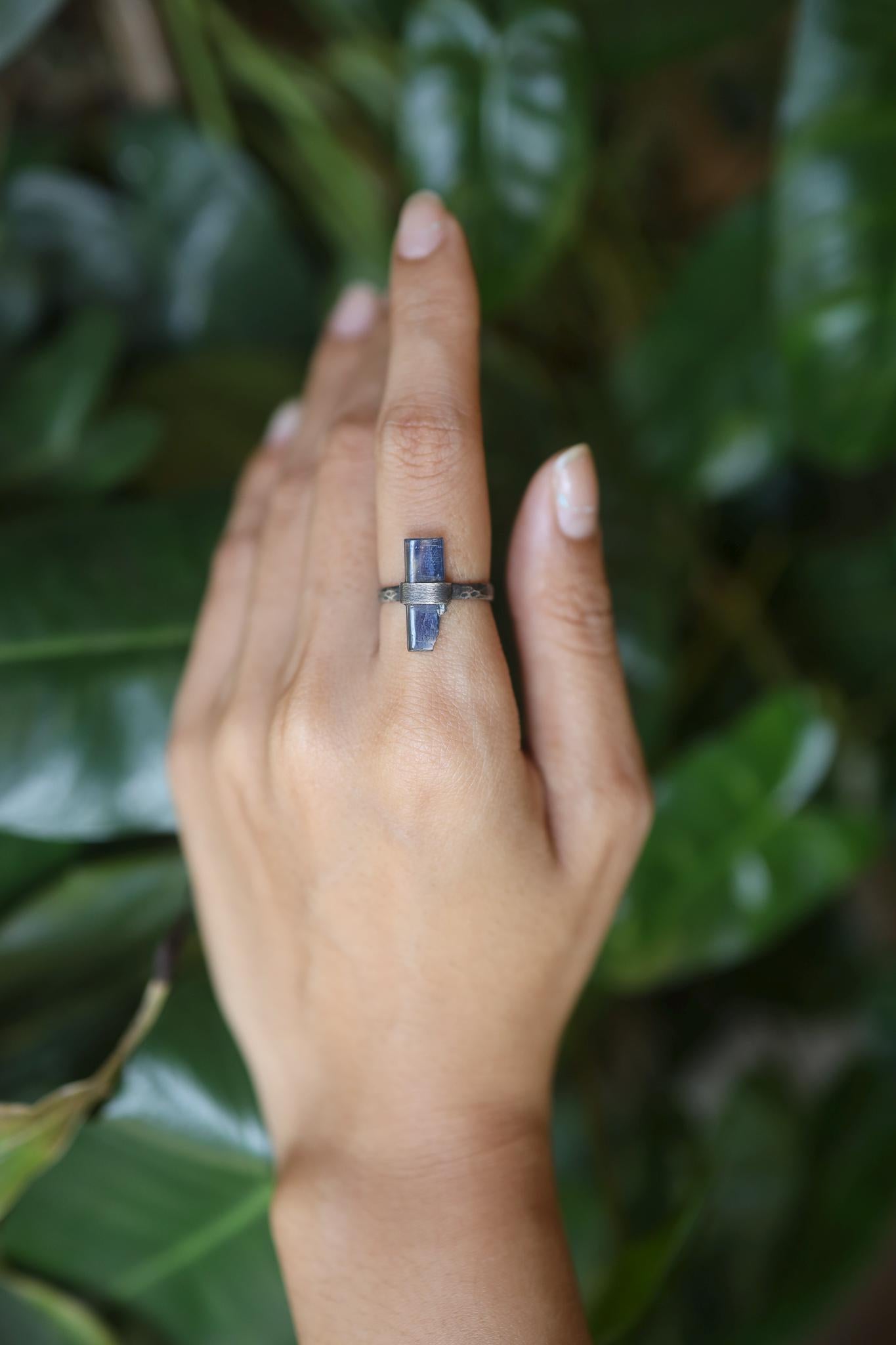 Handmade oxidized 925 sterling silver raw Kyanite ring shown worn on the hand, with deep indigo crystal and hammered band.