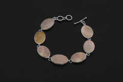 Mother of Pearl bracelet displayed on dark background with oval shell cabochons and sterling silver toggle clasp.