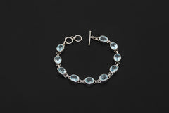 Blue Topaz bracelet displayed on dark background with oval faceted stones and sterling silver toggle clasp.
