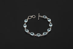 Blue Topaz bracelet displayed on dark background with oval faceted stones and sterling silver toggle clasp.
