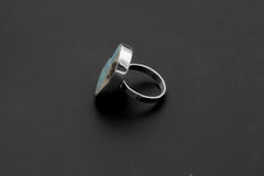 Side view of handmade Larimar ring showing raised freeform stone, polished bezel, and hammered sterling silver band.