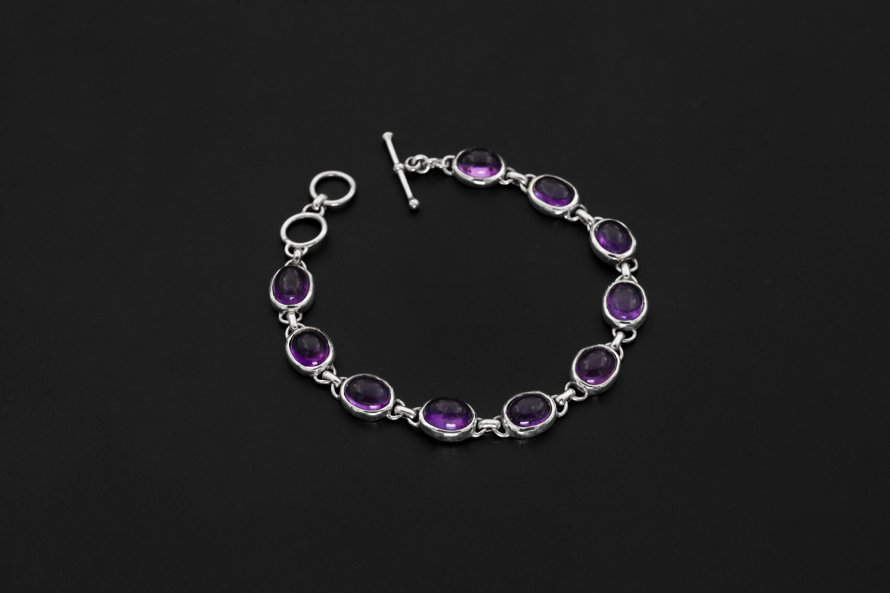 Amethyst sterling silver bracelet shown on dark background beside a ruler with oval purple cabochons and toggle clasp.