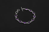 Amethyst sterling silver bracelet shown on dark background beside a ruler with oval purple cabochons and toggle clasp.