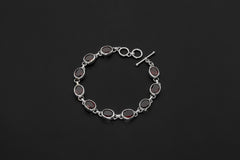 Garnet bracelet displayed on dark background with oval red gemstones in polished sterling silver bezels.