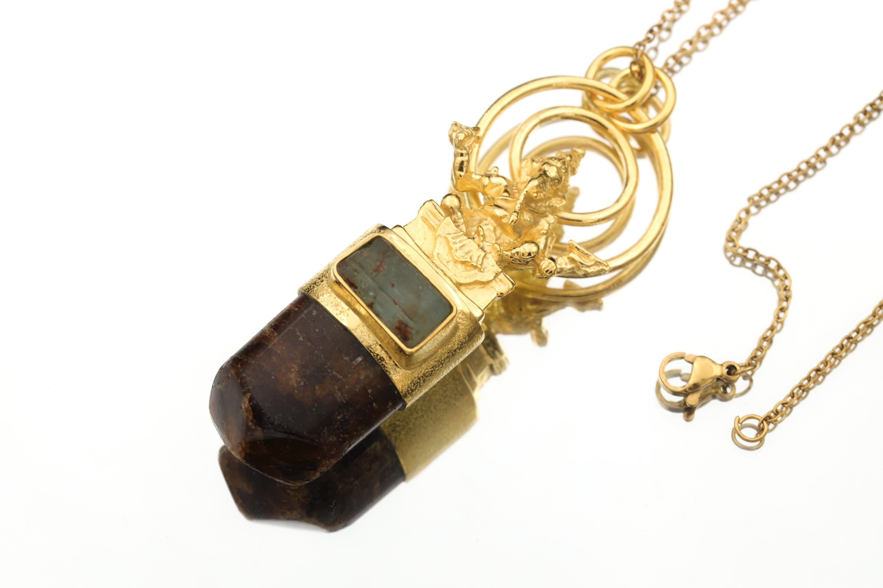 Ganesha Aquamarine Dravite pendant shown on a dark background with 18k gold-plated brass and silver setting.