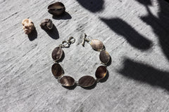 Mother of Pearl bracelet displayed on textured stone with natural oval shell cabochons and polished silver settings.