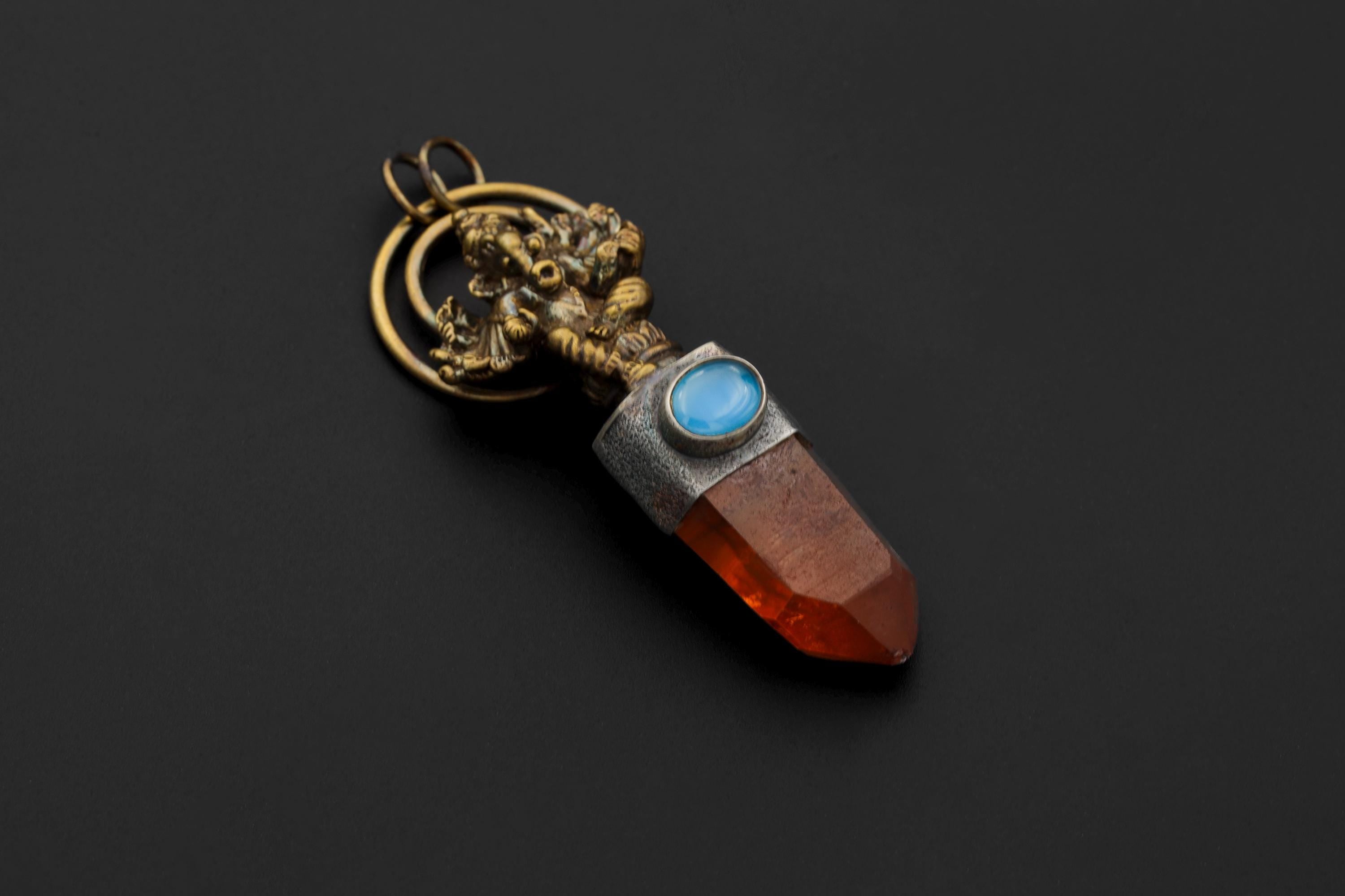 Ganesha Lithium Quartz Aquamarine pendant shown on a dark background with gold-plated brass, oxidized silver, and red Quartz point.