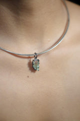 Pendant with raw green tourmaline crystal in oxidized silver claw setting, shown on white background.