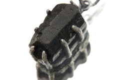 Close-up of raw Black Tourmaline pendant in oxidized sterling silver claw setting, showing natural striations and rugged handmade texture.