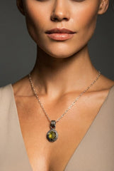 Peridot claw pendant on black background with oxidized sterling silver wire frame and rugged sand-textured finish.