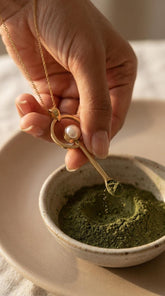 South Sea Pearl gold-plated brass fairy spoon pendant shown being used with green powder in a small ceramic bowl.
