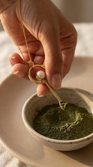 South Sea Pearl gold-plated brass fairy spoon pendant shown being used with green powder in a small ceramic bowl.