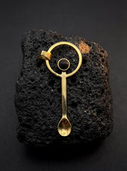 Volcanic stone ritual spoon pendant shown on black lava rock with gold-plated brass and abstract bail detail.