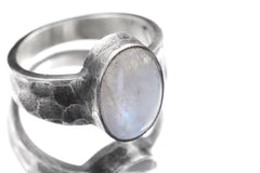 Close-up of AAA Blue Moonstone oval cabochon ring showing thick bezel, oxidized silver, and hammered texture.