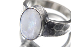 Close-up of AAA Blue Moonstone oval cabochon ring showing thick bezel, oxidized silver, and hammered texture.