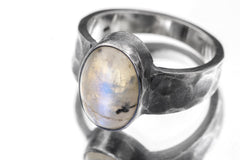 Close-up of AAA Blue Moonstone feldspar ring showing oval cabochon, oxidized silver bezel, and rugged hammered band.