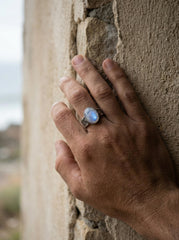 AAA Blue Moonstone ring shown worn outdoors, with luminous oval gemstone and oxidized hammered sterling silver.