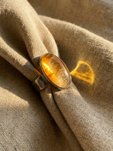 Gold Rutilated Quartz sterling silver ring displayed on fabric with warm golden inclusions and hammered band.