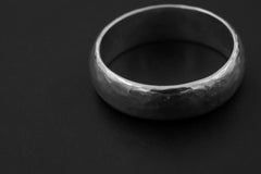 Close view of solid sterling silver band showing softly faceted hammered surface.
