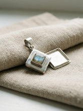 Labradorite locket pendant displayed on linen with polished sterling silver diamond frame and chain.