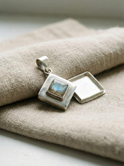 Labradorite locket pendant displayed on linen with polished sterling silver diamond frame and chain.