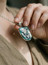 Ancient opalized glass pendant shown worn on model with sterling silver claw setting and iridescent surface.