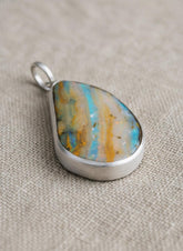 Lightning Ridge Boulder Opal pendant on linen with textured sterling silver bezel, freeform opal shape, and soft spectral colour play.