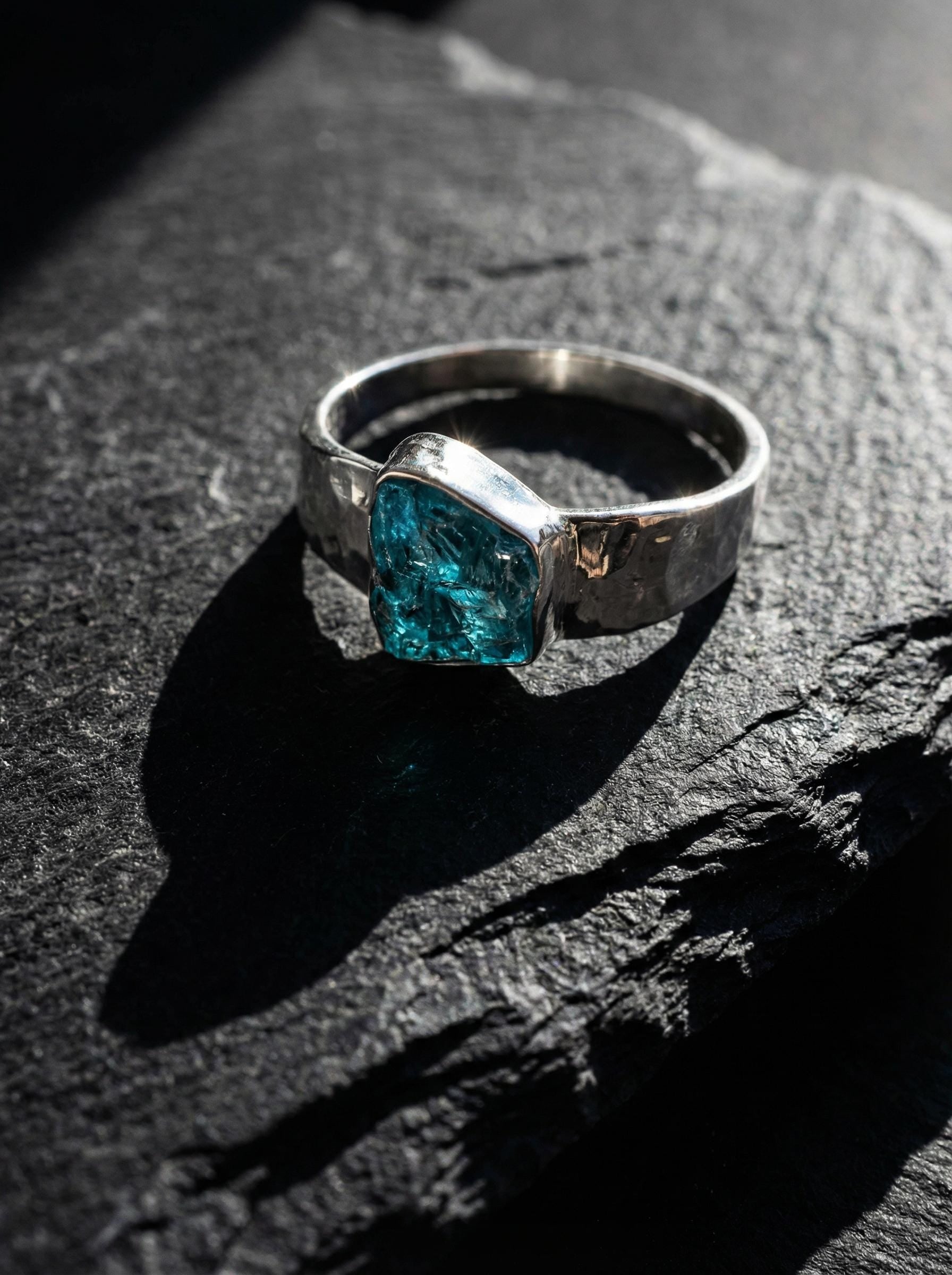 Blue Apatite Textured Silver Ring shown on dark rock with semi rough blue crystal and handmade sterling silver band.