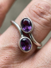 Amethyst sterling silver wrap ring shown worn on hand with two oval purple gemstones.