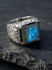 Labradorite sterling silver statement ring shown on dark stone with blue flash square gemstone and scale texture.