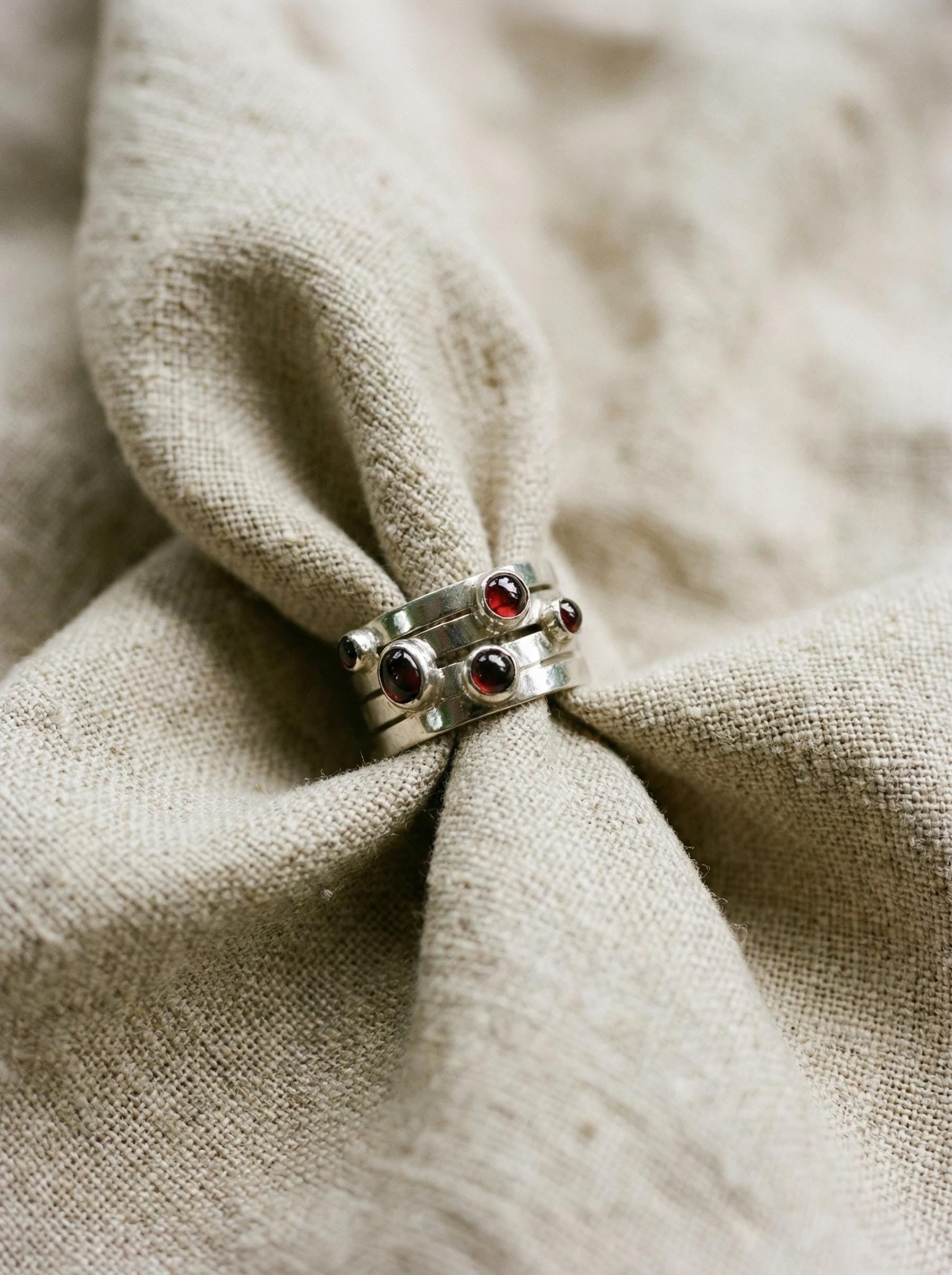 Five Stone Garnet Unity Ring displayed on fabric with polished sterling silver and deep red cabochons.