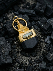Buddha Black Tourmaline pendant displayed on dark stone with gold-plated brass and silver detail.