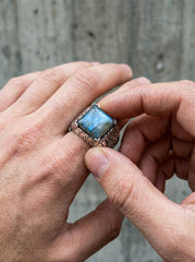 Labradorite ring shown held in hand with wide textured sterling silver band and blue flash stone.
