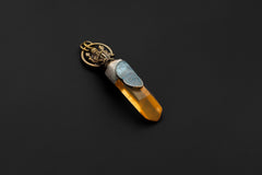 Ganesha talisman pendant shown on dark background with brass figure, Aquamarine, and golden Quartz point.