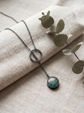 Turquoise lariat necklace displayed on linen with oxidized sterling silver chain and adjustable loop closure.