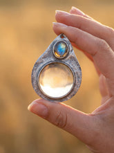 Labradorite magnifying glass pendant shown held in hand with sunlight through 5x lens and oxidized sterling silver frame.