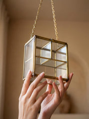 Large rectangular glass brass display box held near window light with clear panels and hanging chain.
