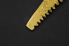 Close view of serrated gold-plated brass cutter spoon pendant with textured handmade surface.