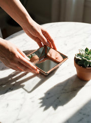 Square copper mirror shown in sunlight with angled panels reflecting light across a tabletop surface.