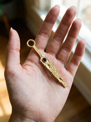 Gold-plated Garnet cutter spoon pendant held in hand as a functional ritual talisman.