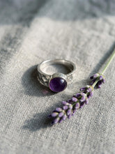 Harmonious Amethyst Essence Ring shown on fabric with hammered sterling silver band and round purple gemstone.