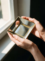 Handmade brass mirrored tray held near a window, showing angled glass panels and warm metal frame.