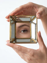 Handmade brass mirror geometric tray held in hand, showing angled reflective panels and square pyramid-style shape.