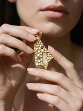 Gold-plated Double Amethyst cast pendant held near face with sculptural triangular ritual form.